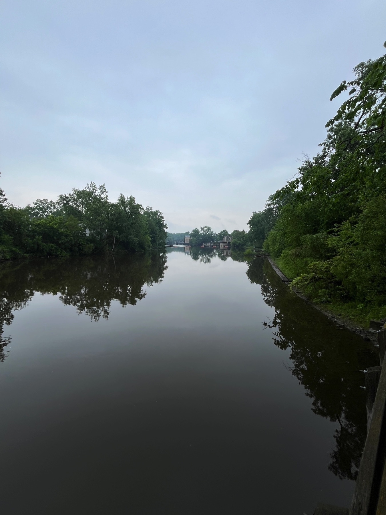 A calm river flows through a green, tree-lined landscape under a cloudy sky.