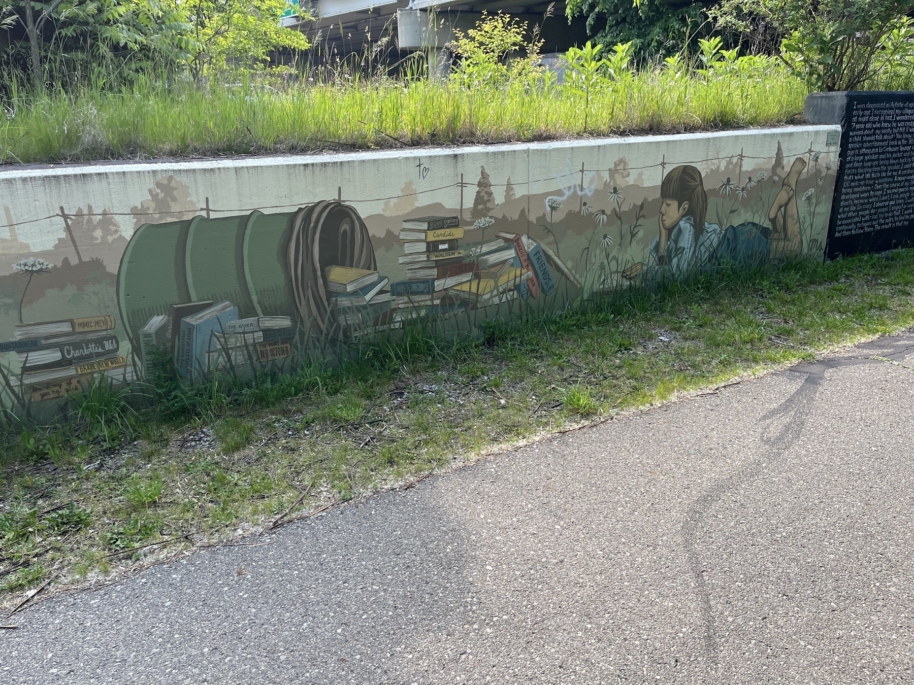 A mural depicts a girl reading a book, surrounded by stacks of books, against a backdrop of outdoor scenery.