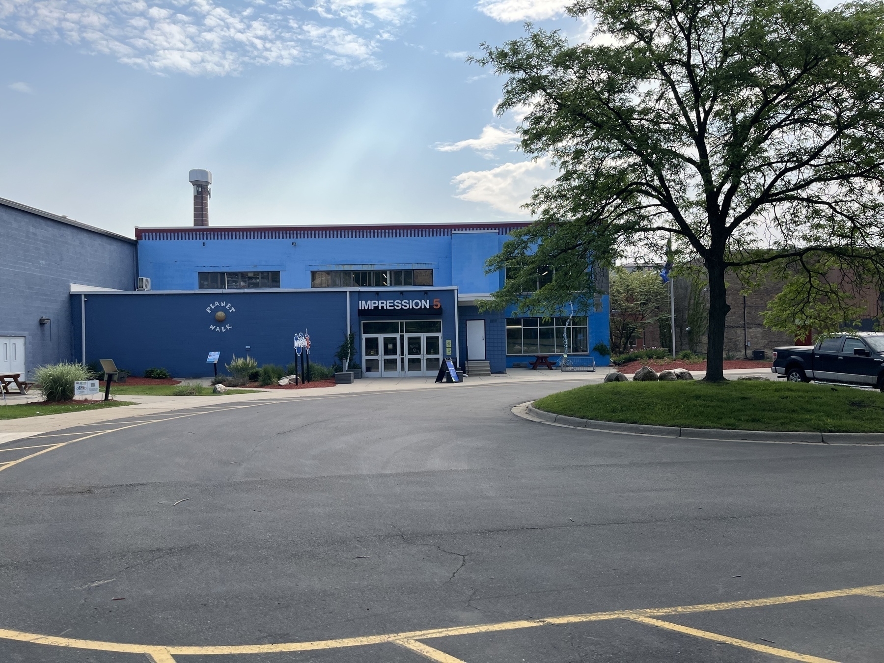 A blue building with a sign reading Impression 5 is surrounded by a parking area and a tree.