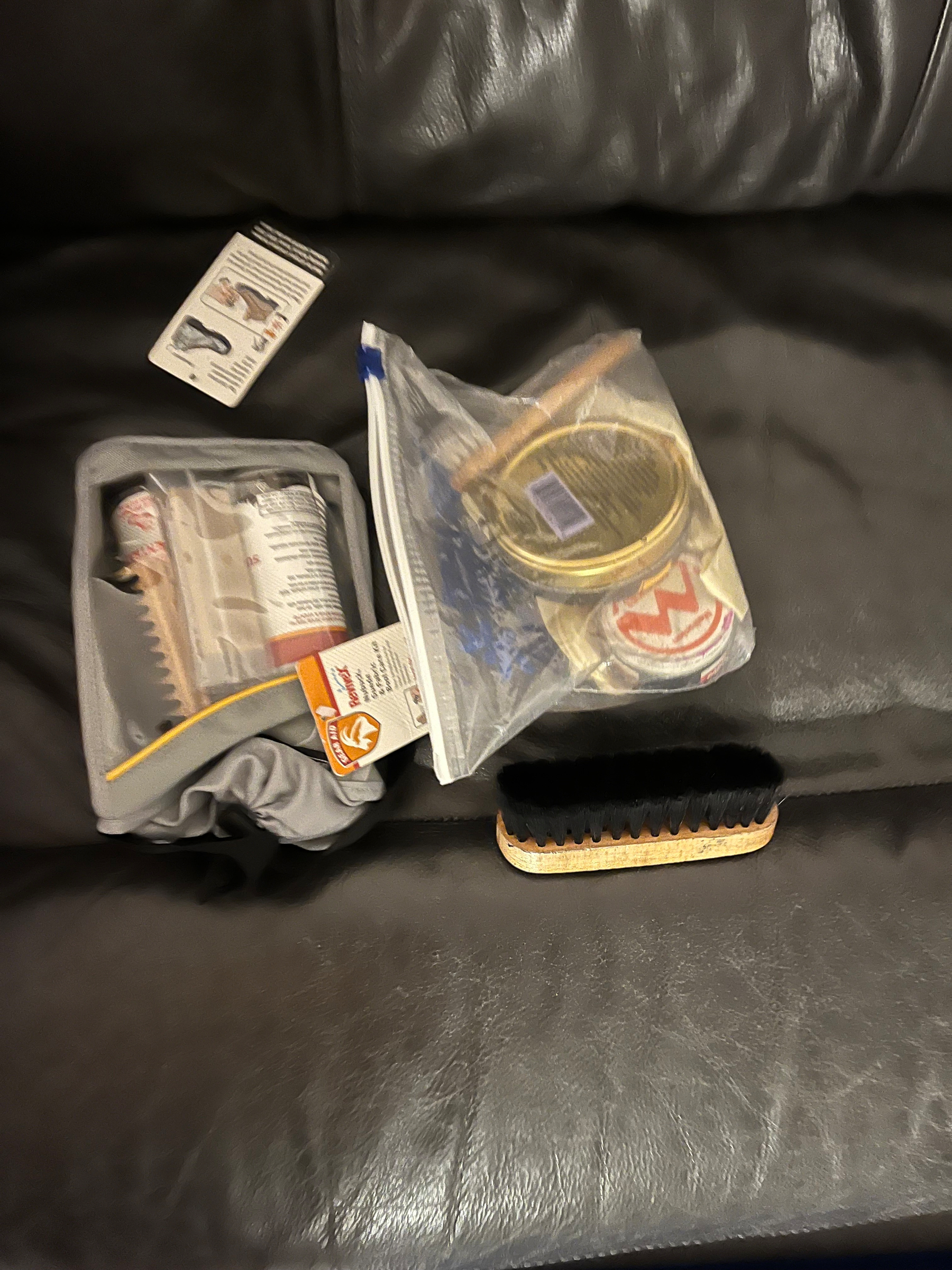 Various shoe care items, including brushes, polish, and a shoehorn, are placed on a dark leather surface.