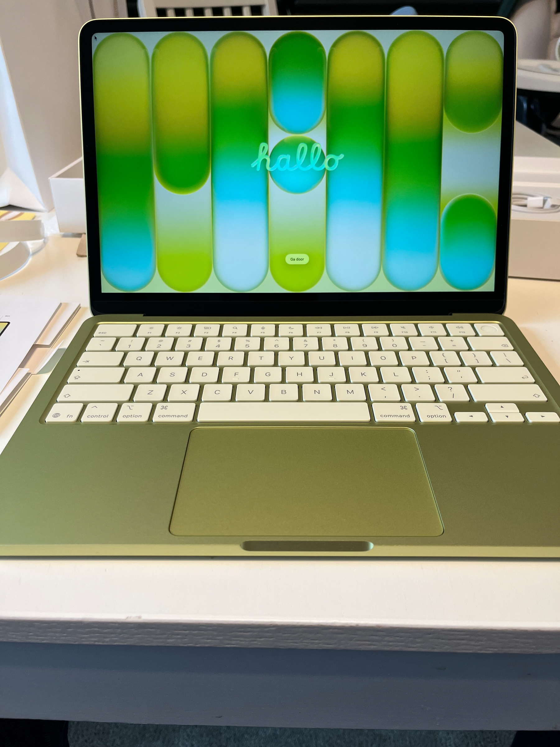A picture of a new citrus Macbook Neo sitting on a white dining room table