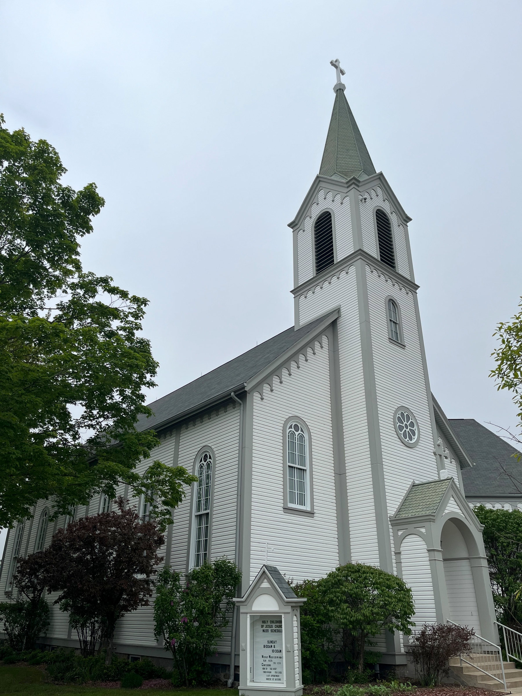A white church with a tall steeple is surrounded by greenery.