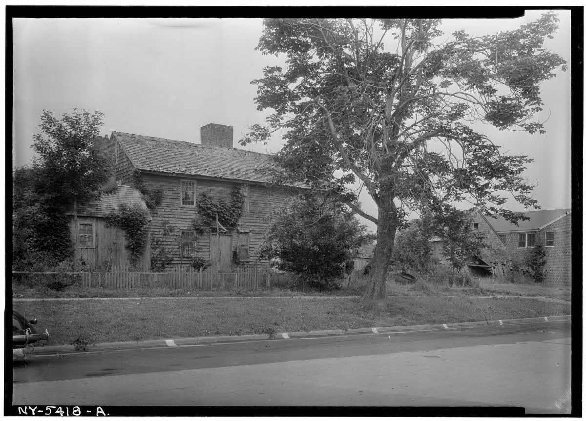 Exterior, general view from southeast (clock shop at left). Dominy House, North Main Street, East Hampton, Suffolk County, NY. Photo by Stanley P. Mixon, July 20, 1940. [hdl.loc.gov/loc.pnp/h...](http://hdl.loc.gov/loc.pnp/hhh.ny0772/photos.123498p.) A historic black-and-white photograph (labeled NY-5418-A) of a two-story wooden clapboard house with a large mature tree in the front yard. Overgrown vines climb parts of the exterior facade and an adjoining wooden shed on the left. A simple wooden picket fence borders the front of the property alongside a paved street.