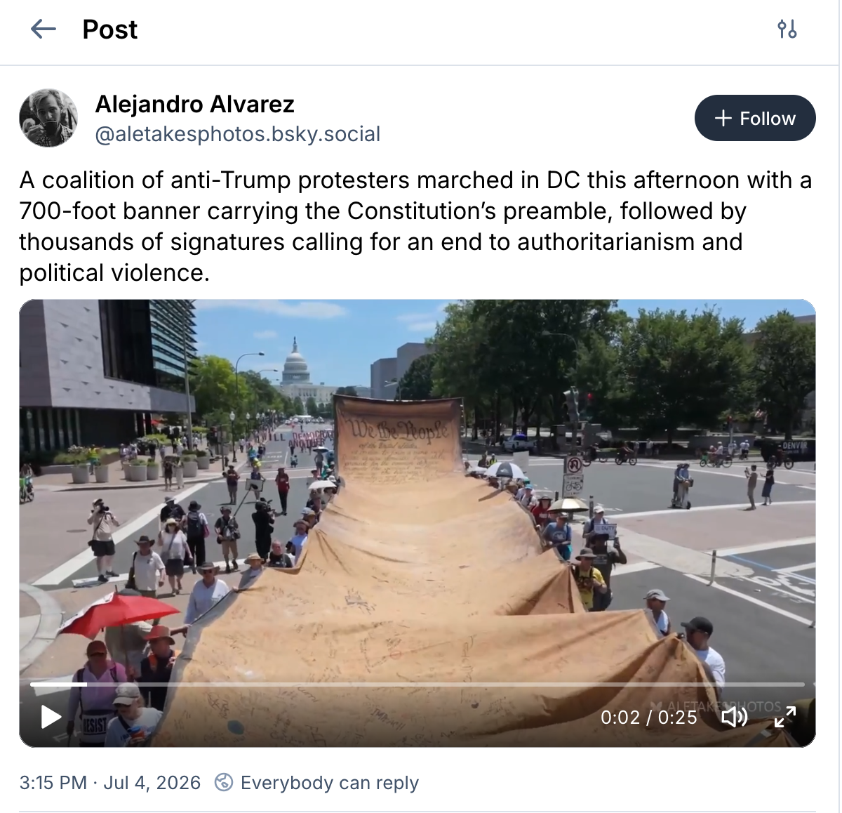A screenshot of a social media post from July 4, 2026, by Alejandro Alvarez. The text states that a coalition of anti-Trump protesters marched in Washington, D.C., with a 700-foot banner featuring the Constitution’s preamble and thousands of signatures. The video still shows a high-angle view of a city street leading toward the U.S. Capitol dome in the background. Protesters are holding the edges of an enormous, parchment-colored fabric banner, with the front section stylized to read “We the People” in large cursive script and the rest of the long trailing fabric covered in handwritten messages and signatures.